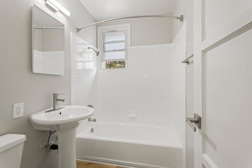 A white bathroom with a sink, mirror, and bathtub.