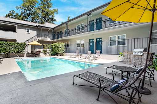 A yellow umbrella is on a table next to a pool.