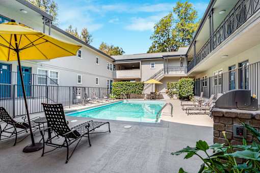 A pool area with chairs and a yellow umbrella.