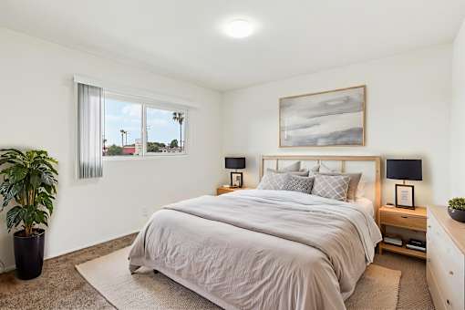 A bedroom with a large bed, a potted plant, and a painting on the wall.