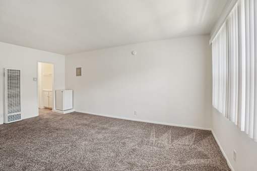 A room with a carpeted floor and a window with blinds.