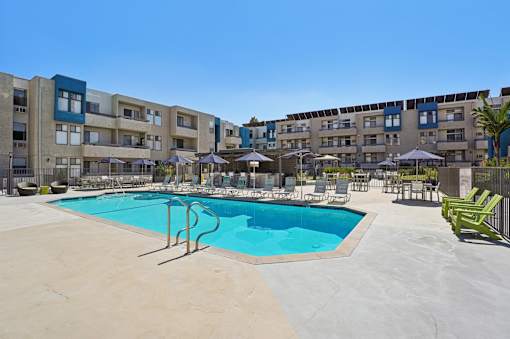 A swimming pool in a courtyard surrounded by chairs and umbrellas.