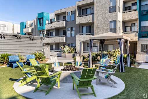 a patio with rocking chairs and a fire pit in front of an apartment building