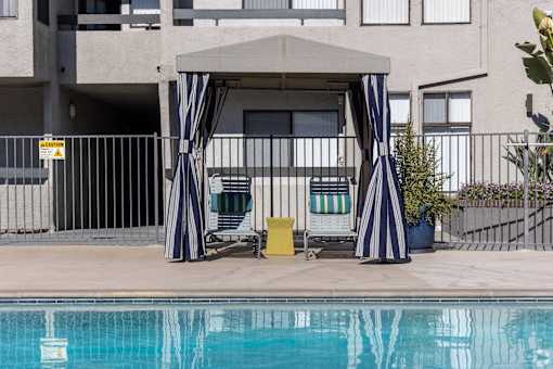 a pool cabana with two chairs next to a swimming pool