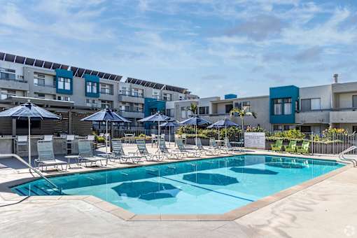 a swimming pool with chairs and umbrellas in front of an apartment building