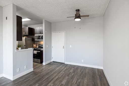 an empty living room with a ceiling fan and a kitchen