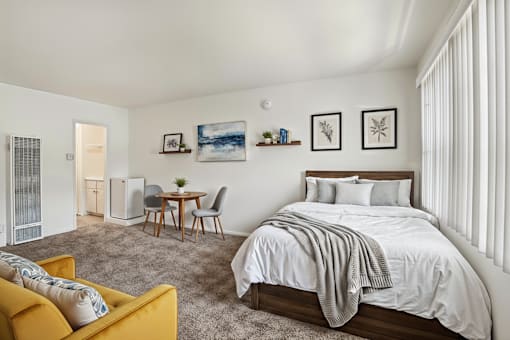 A bedroom with a bed, a table and chairs, and a yellow couch.