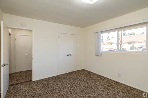 A room with carpeted floor, two doors, and a window.