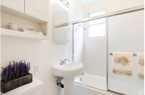 A white bathroom with a white sink and a white towel hanging on the shower door.