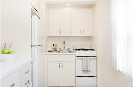 A white kitchen with a refrigerator, sink, and stove.
