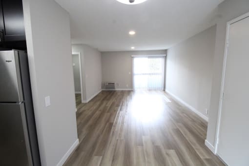 an empty living room with wood flooring and a refrigerator