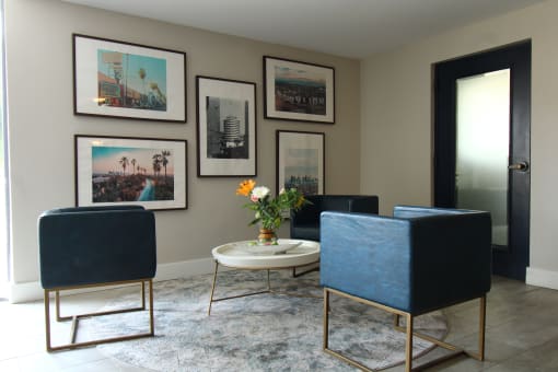 a living room with blue chairs and a table and pictures on the wall