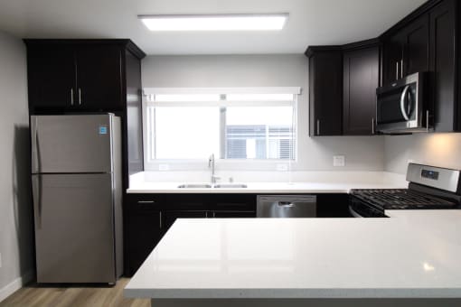 A kitchen with black and white counters and a stainless steel refrigerator