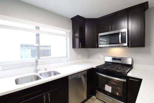 A kitchen with black cabinets and stainless steel appliances and a window