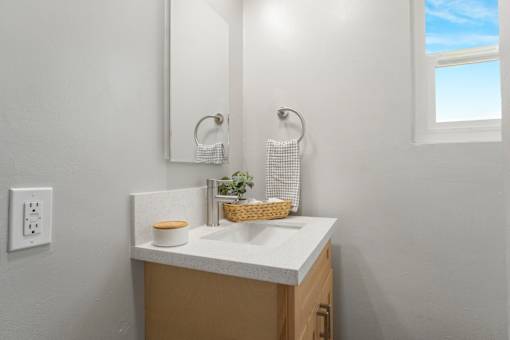 A bathroom with a white countertop and a basket of greenery on it.