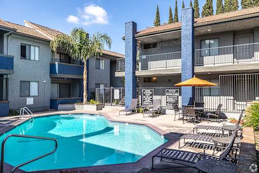 A swimming pool surrounded by chairs and umbrellas in front of apartment buildings.