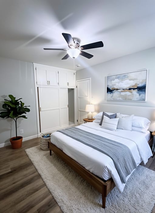 A bedroom with a bed, a ceiling fan, and a painting on the wall.