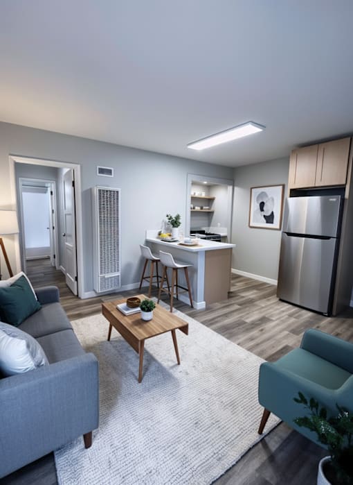 A modern living room with a grey sofa, a wooden coffee table, and a kitchen area in the background.