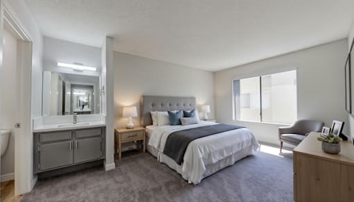 A bedroom with a large bed, a chair, and a vanity with a mirror.