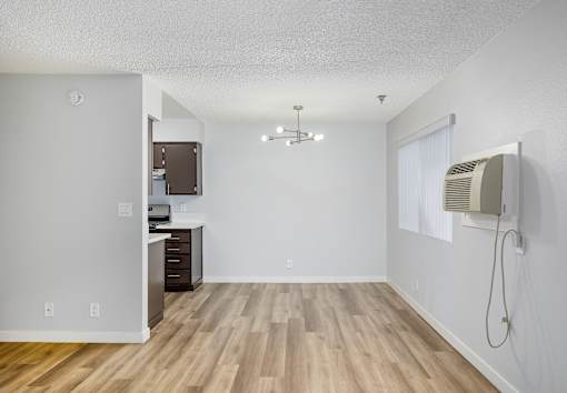 A room with a wooden floor and a white wall with a window and a fan.