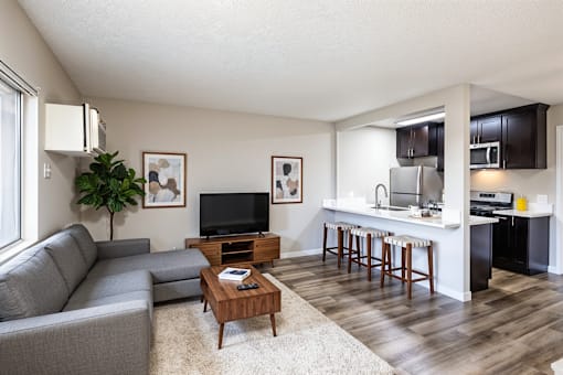 A living room with a grey couch, a wooden coffee table, and a kitchen area in the background.