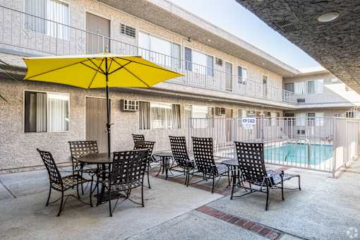A yellow umbrella is on a table with chairs around it.