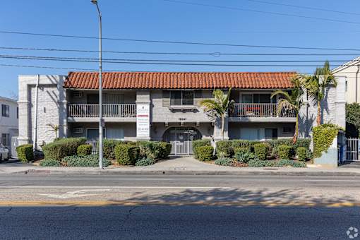 A building with a red tile roof is surrounded by green bushes.