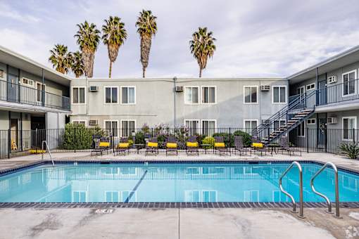 A swimming pool in front of a building with palm trees in the background.
