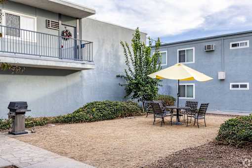 A patio with a table and chairs and a yellow umbrella.