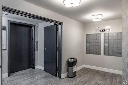 A room with a trash bin and a wall of mailboxes.