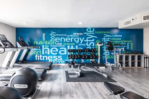 A gym with a variety of equipment and a wall with words related to fitness.