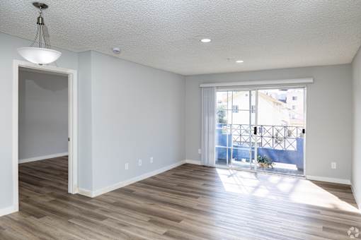 A room with a wooden floor and a sliding glass door leading to a balcony.