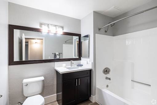 A bathroom with a toilet, sink, mirror, and bathtub.