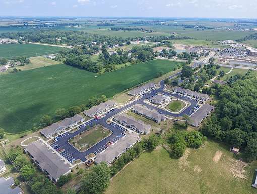 A bird's eye view of a residential area with a large green field and a roundabout in the center.