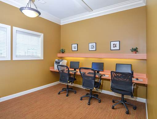 A room with four chairs and a desk with a laptop and a monitor.