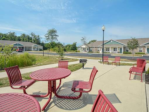 A sunny day at a park with red chairs and tables.