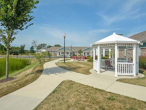 A white gazebo is surrounded by a paved walkway in a grassy area.