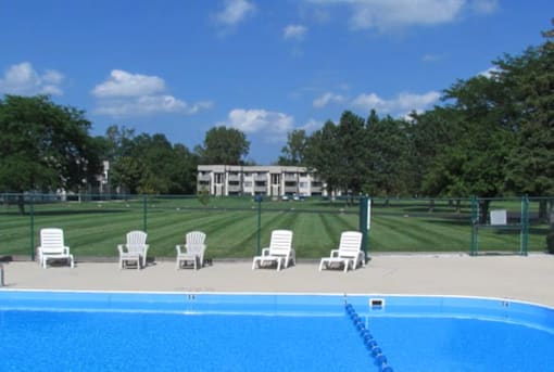 A pool with chairs around it and a building in the background.