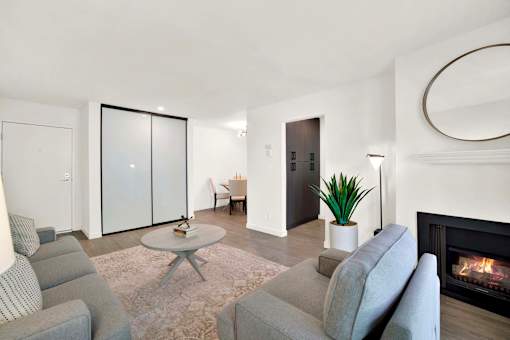 A living room with a grey couch, a coffee table, a fireplace, and a plant at Westwood Riviera Apartments, Los Angeles, 90024