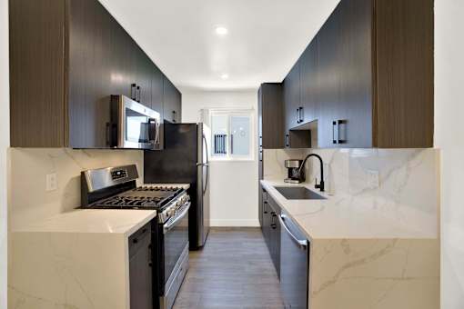 A modern kitchen with dark brown cabinets and marble countertops at Westwood Riviera Apartments, California