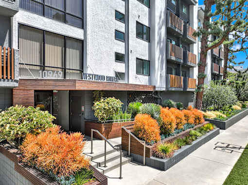 A modern building with a balcony and a row of orange plants in front. at Westwood Riviera Apartments, Apartments, Los Angeles, CA