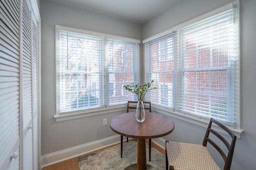 A room with a table and chairs and a vase of flowers on it.