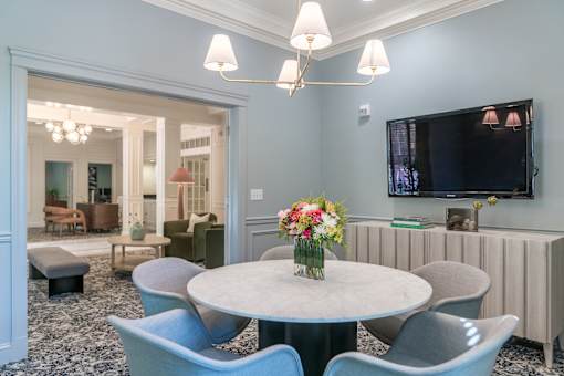 A living room with a round table and chairs, a television, and a chandelier.