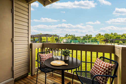 A balcony with a table and chairs overlooking a green field.