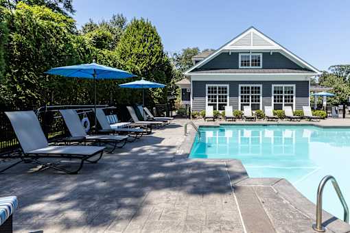 A pool area with lounge chairs and umbrellas in front of a house.