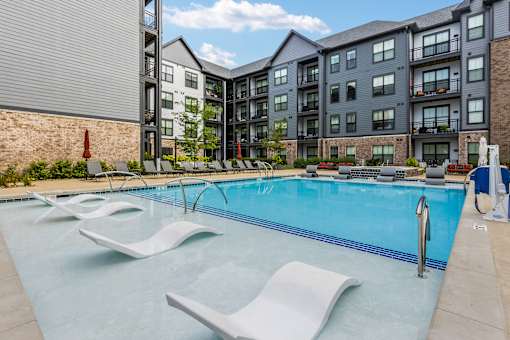 A swimming pool with lounge chairs and a building in the background.