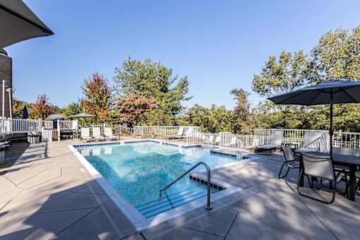A small pool surrounded by a patio with chairs and an umbrella.