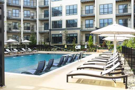 A pool with lounge chairs and umbrellas in front of apartment buildings.