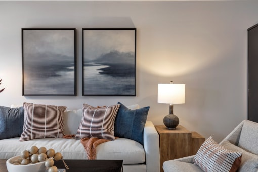 a living room with two paintings on the wall and a white couch with pillows at The Austin Apartment Homes, Deptford, 08096