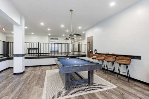 A pool table is in the middle of a room with a bar in the background.
